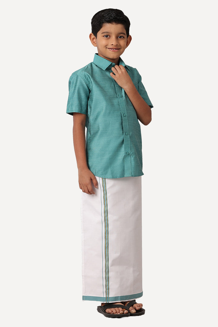 A boy wearing a green shirt and white dhoti with green borders standing against a white background.
