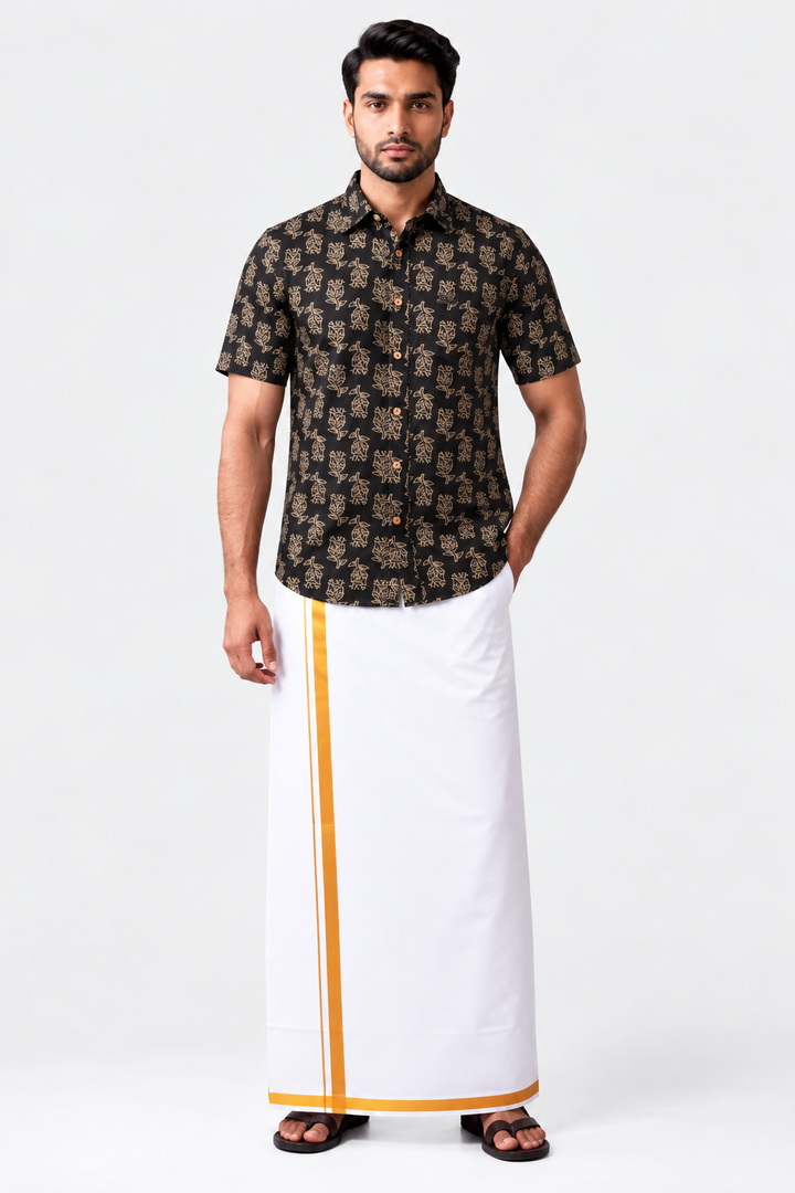 A man modeling a traditional Indian outfit consisting of a black short-sleeve shirt with a gold floral pattern and a white drape (kurtu) with a gold border, against a plain white studio background.