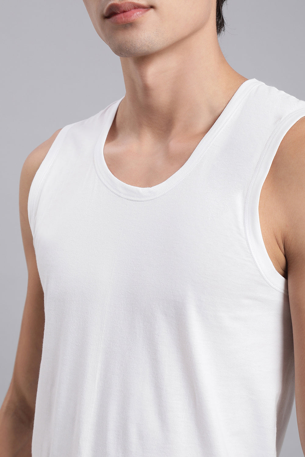 Man wearing a white sleeveless vest against a gray background