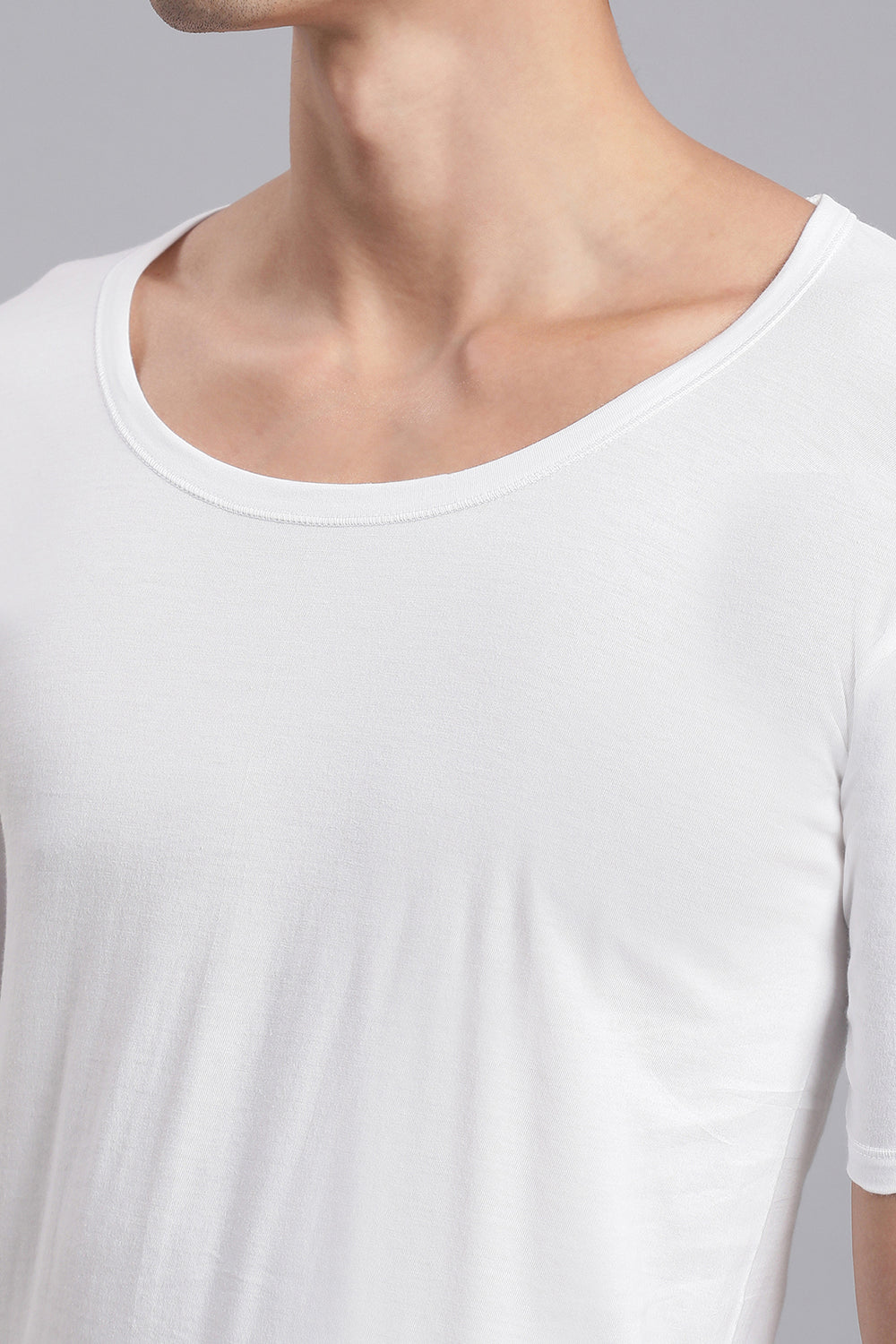 Close-up of a person wearing a plain white vest against a gray background