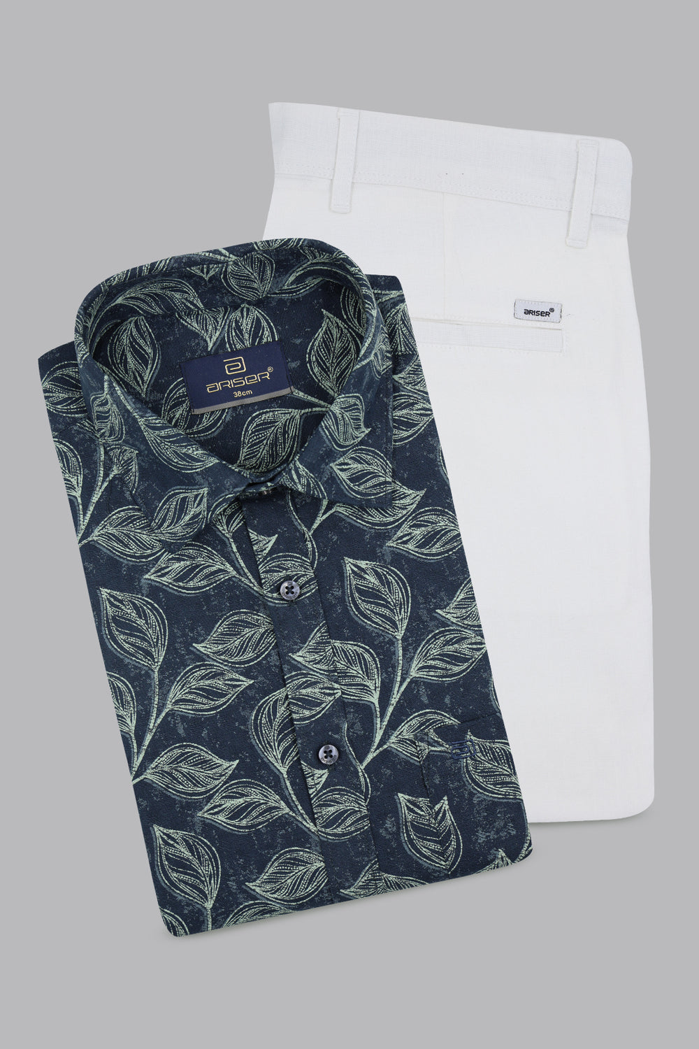 Folded navy blue shirt with green leaf pattern next to a white pants on a gray background