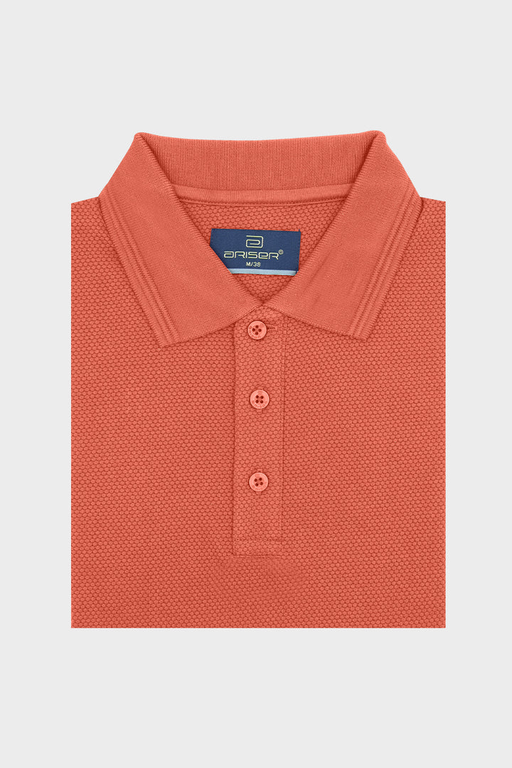 A folded coral orange polo shirt with a textured micro-pique knit, featuring a classic collar, three buttons, and a blue 'cromare' brand label inside the collar, set against a light gray background.