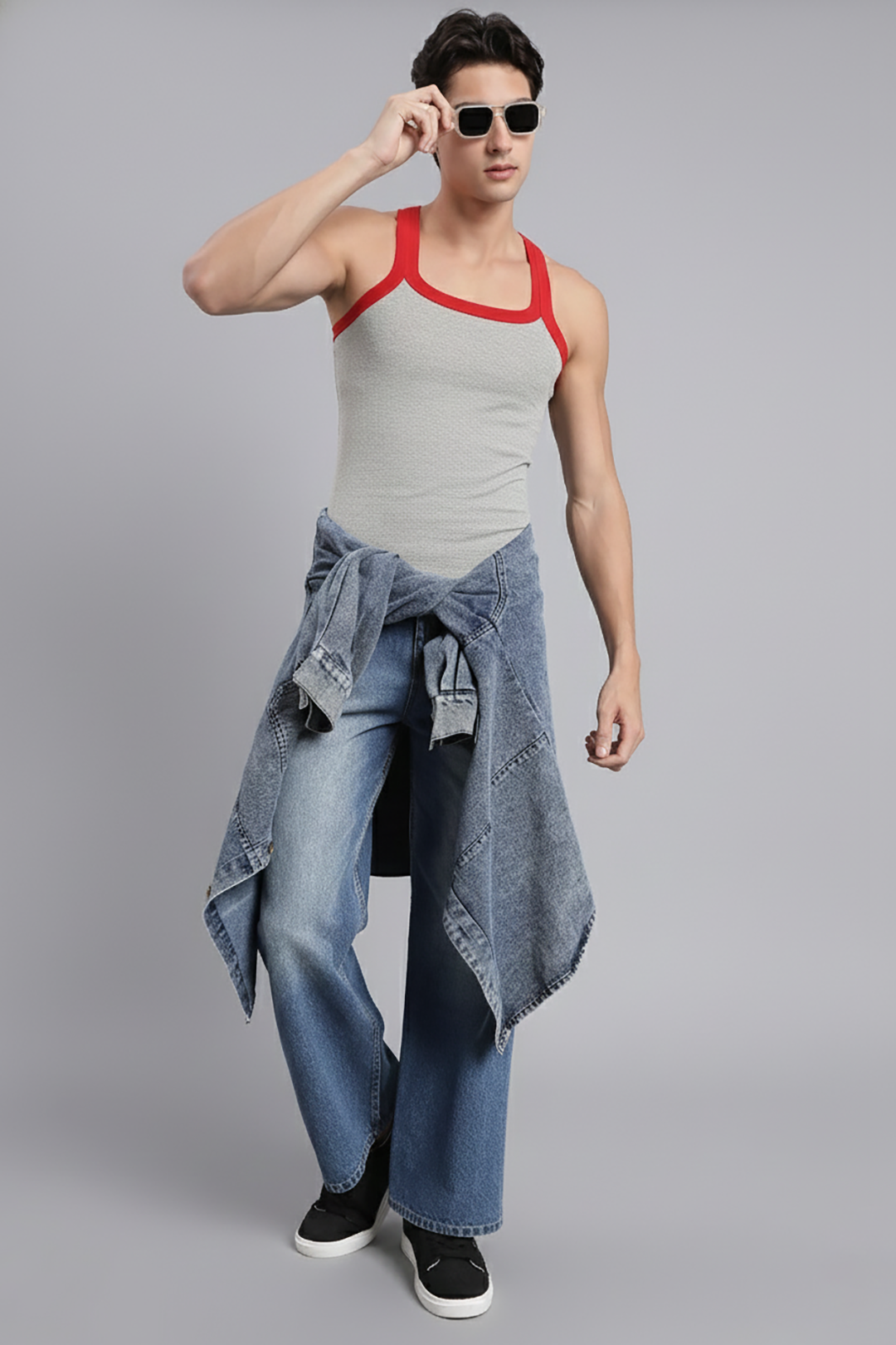 Man wearing a gray tank top with red straps and blue jeans on a gray background