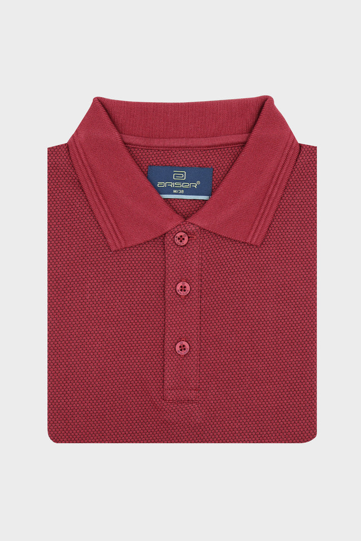 A folded red polo shirt with a textured micro fabric, featuring a classic collar and three-button placket, displayed on a light gray background.
