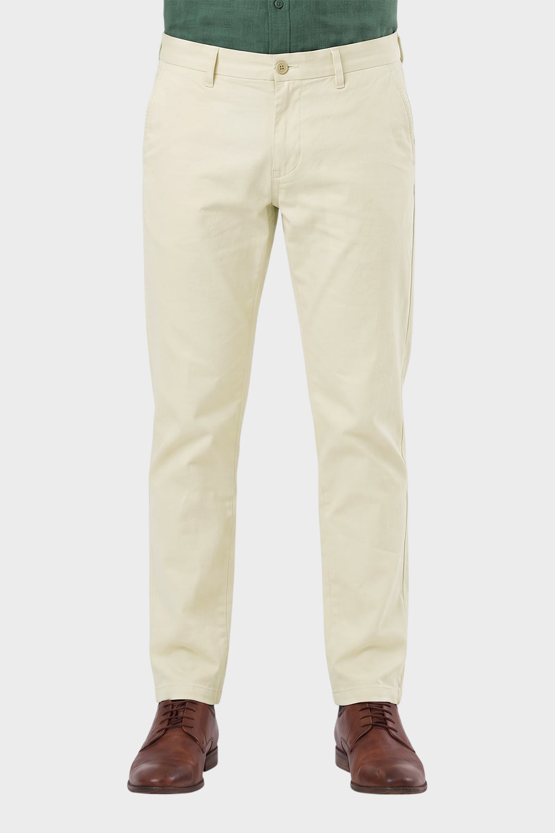 A person wearing light cream chino pants with a green shirt and brown leather dress shoes, shown from the waist down on a light gray background.