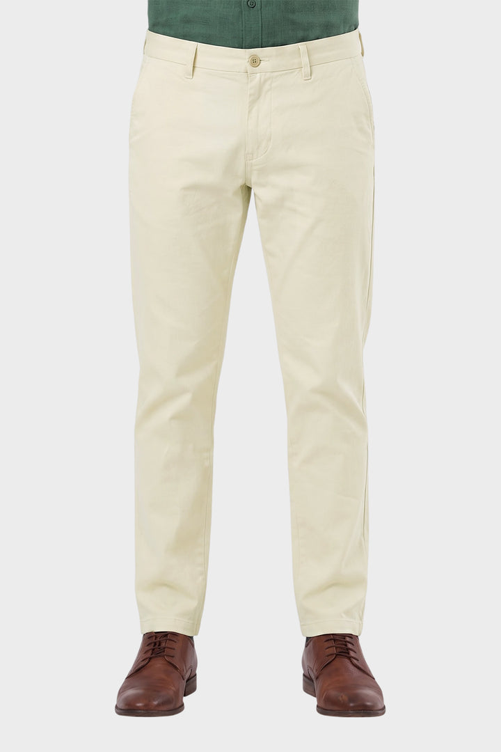 A person wearing light cream chino pants with a green shirt and brown leather dress shoes, shown from the waist down on a light gray background.