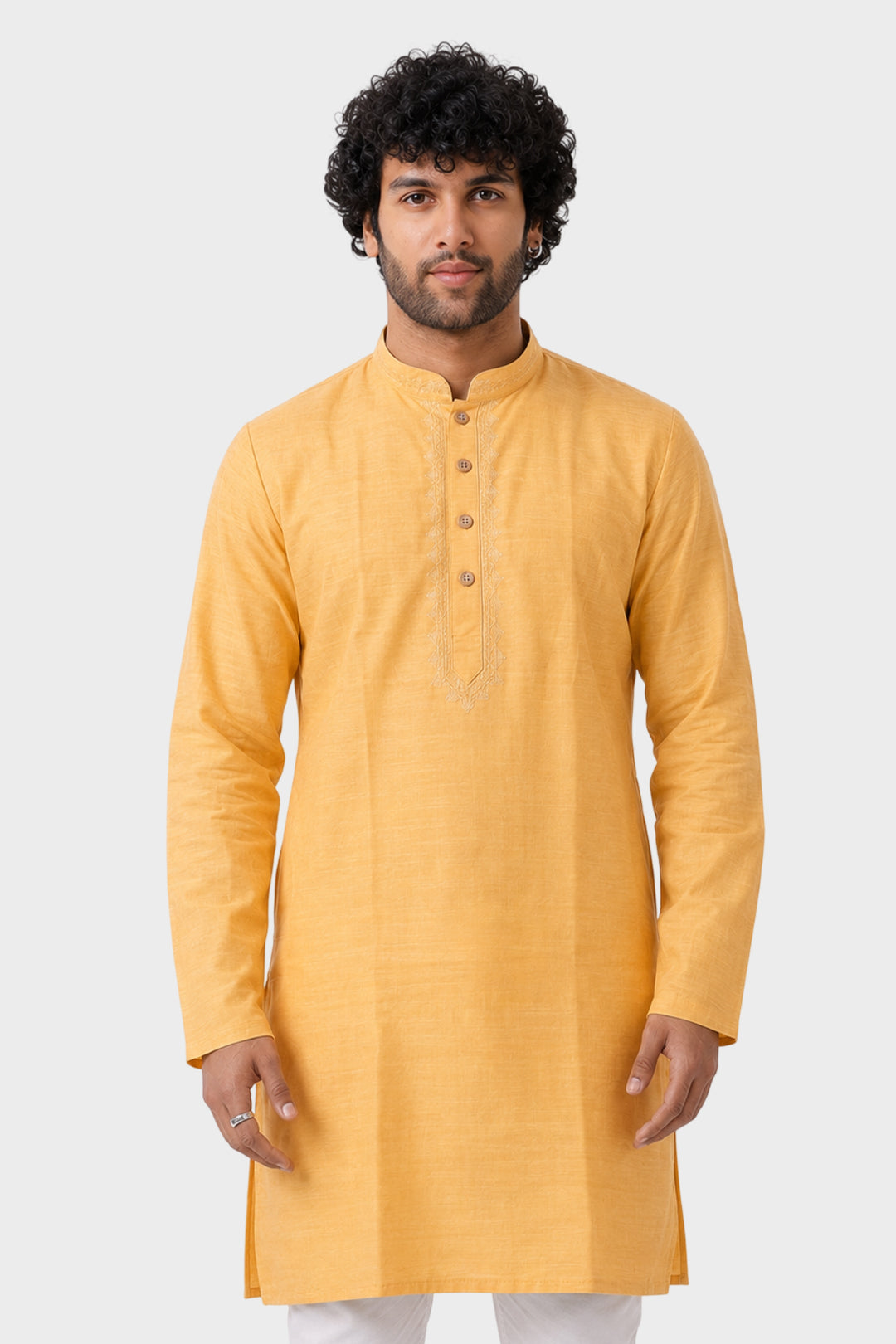 A man wearing a mustard yellow long-sleeve kurta with a mandarin collar and three-quarter button placket, paired with white trousers, set against a solid light gray background.