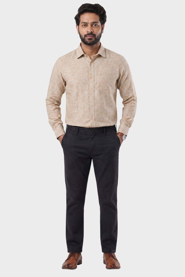 A man wearing a beige long-sleeve textured button-down shirt, black trousers, and brown dress shoes, standing against a light gray studio background.