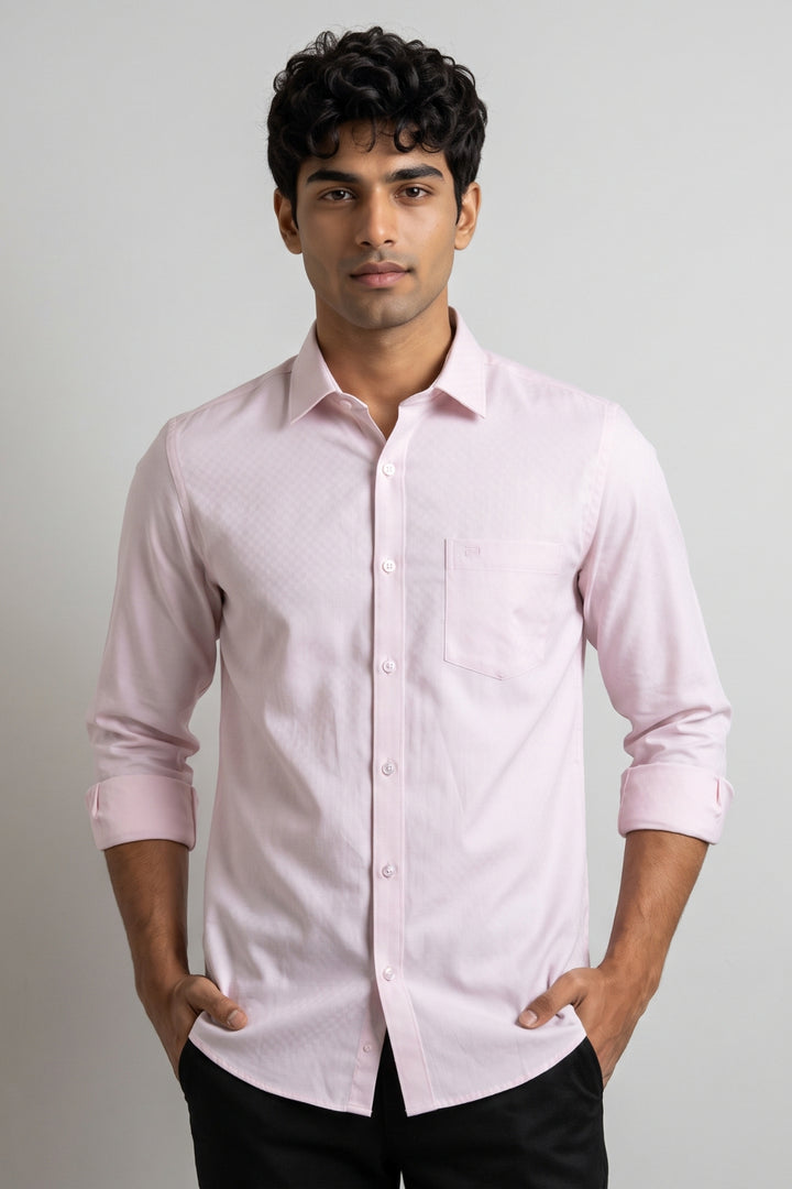 A man wearing a pink long-sleeve button-down shirt with a subtle textured pattern, paired with black trousers, standing against a neutral light gray background.