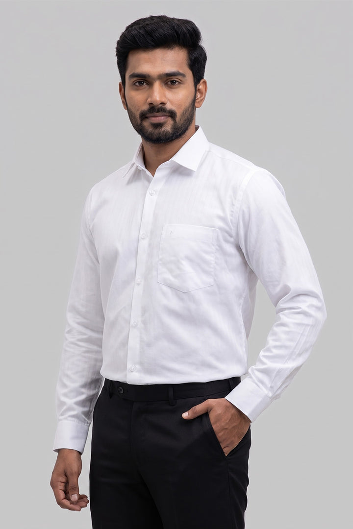 A man wearing a white long-sleeve button-down dress shirt with black trousers, standing against a solid gray studio background.