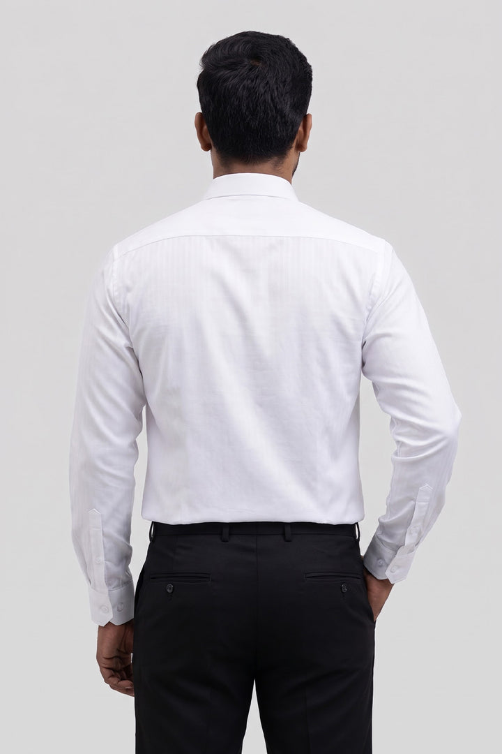 A man viewed from behind wearing a white long-sleeve dress shirt and black trousers, standing against a light gray studio background.