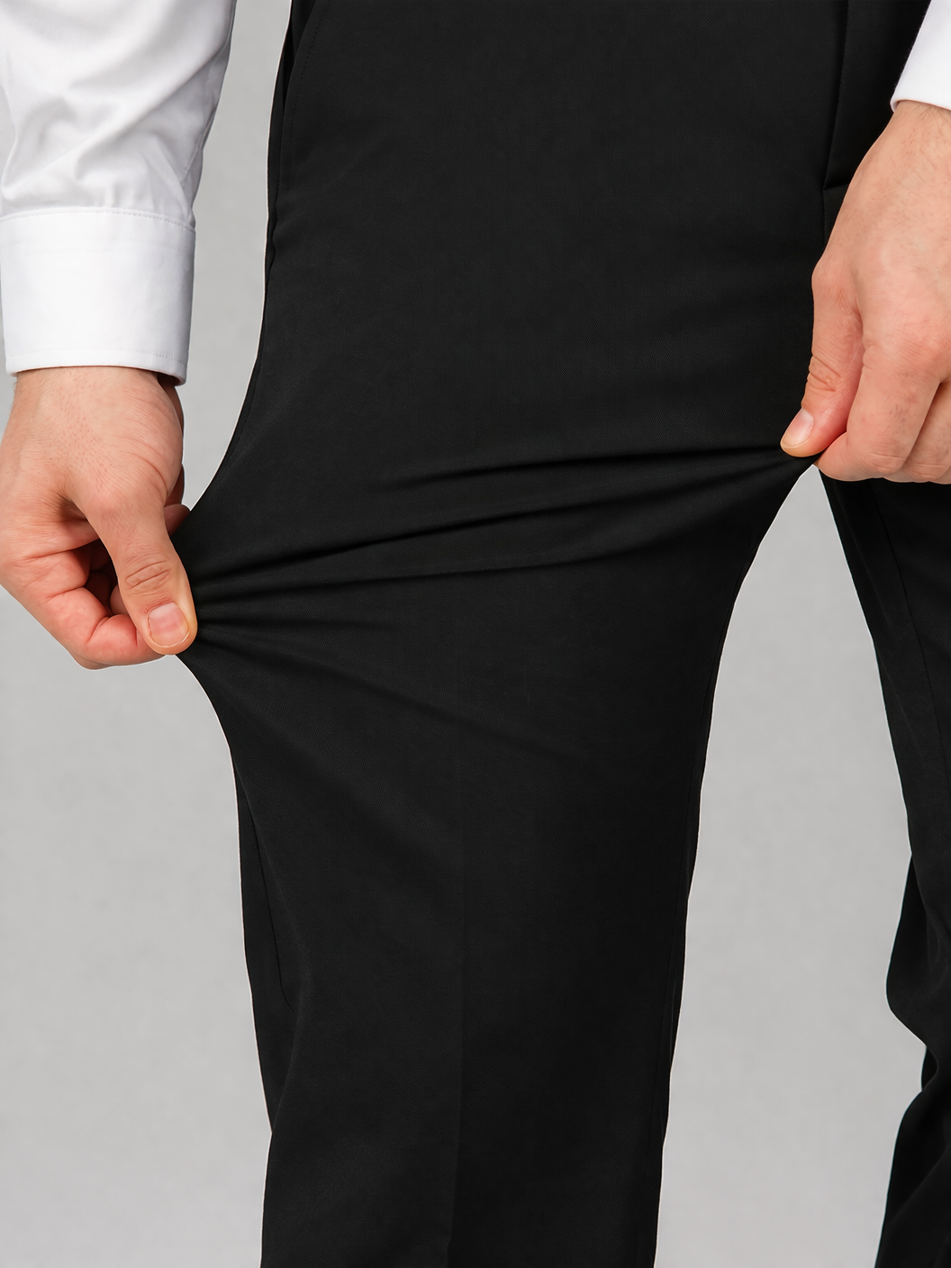 Person holding a black pants to show its stretchiness on a gray background
