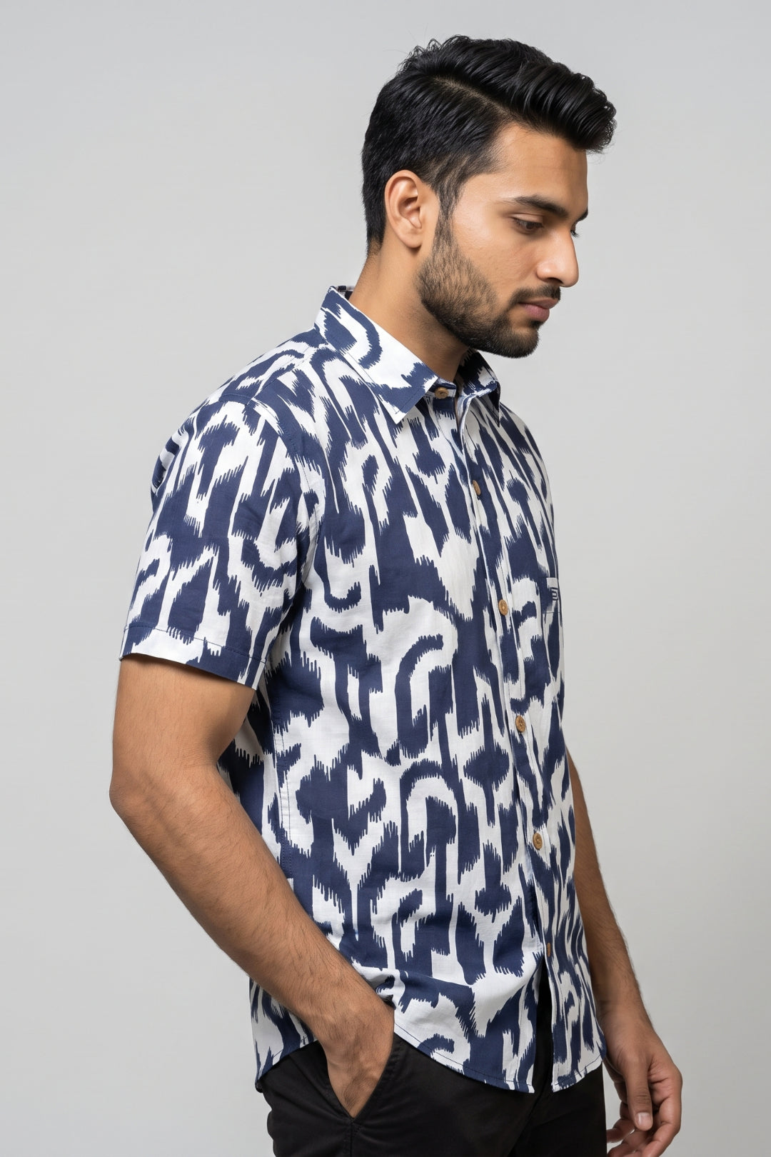 A man wearing a short-sleeve button-up shirt with a navy blue and white ikat pattern, posed in profile against a light gray studio background.