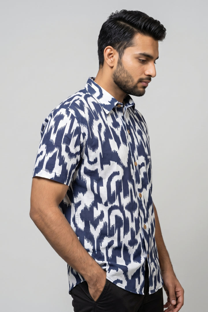 A man wearing a short-sleeve button-up shirt with a navy blue and white ikat pattern, posed in profile against a light gray studio background.