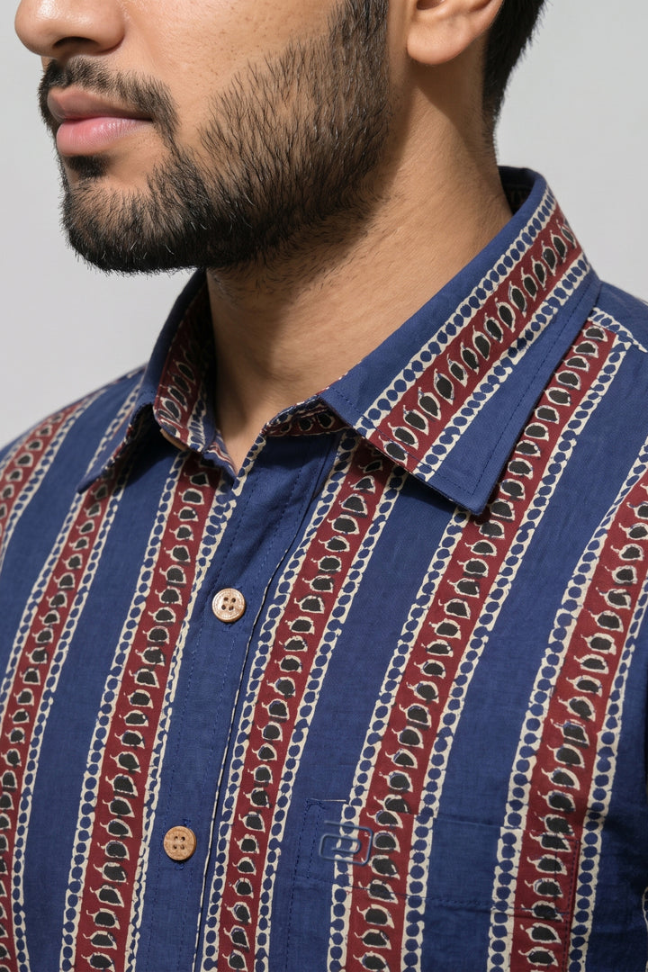 Close-up of a man wearing a blue button-up shirt with vertical red and cream paisley patterned stripes.