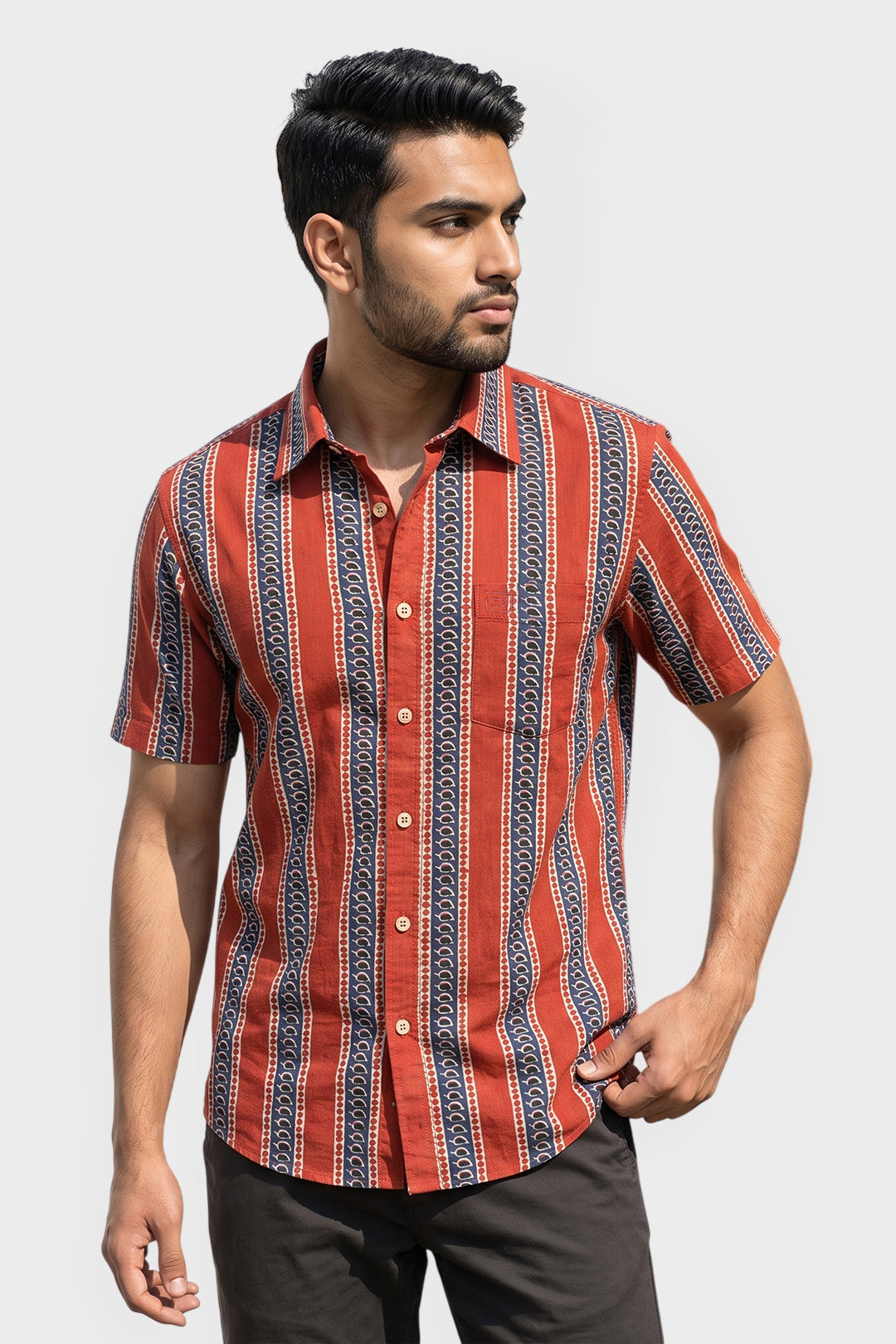 A man wearing a short-sleeve button-up shirt with vertical red, orange, and navy blue patterned stripes, paired with dark brown trousers, set against a plain light gray background.