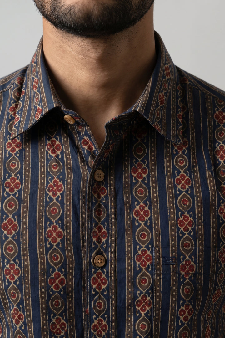 Close-up of a man wearing a patterned button-down shirt with vertical stripes and red floral motifs on a navy and brown base.