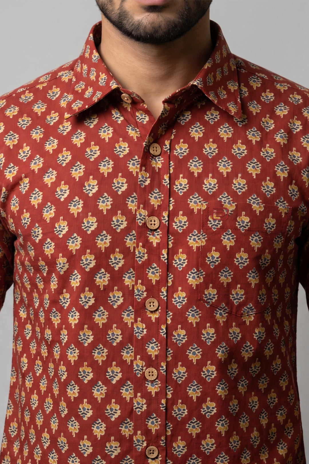 A close-up of a man wearing a rust-red button-up shirt with a repeating yellow, blue, and white floral pattern.