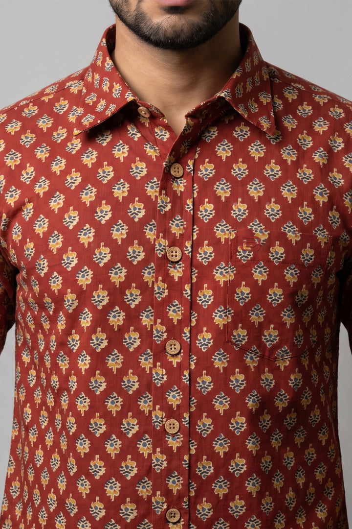 A close-up of a man wearing a rust-red button-up shirt with a repeating yellow, blue, and white floral pattern.