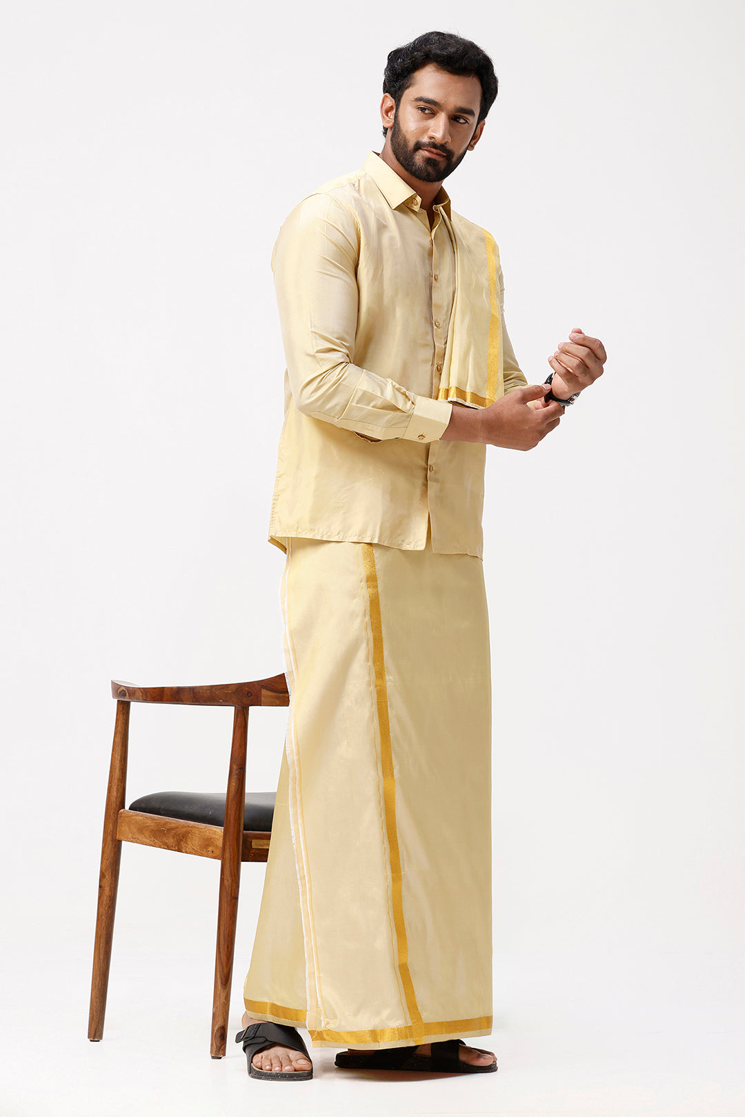 Man wearing a traditional beige outfit with dark gold accents on a white background