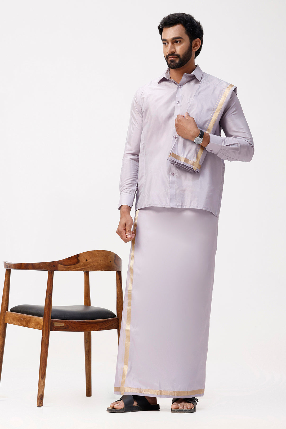 Man wearing a traditional outfit with a violet dhoti and light-coloured shirt, holding a folded fabric, on a white background.