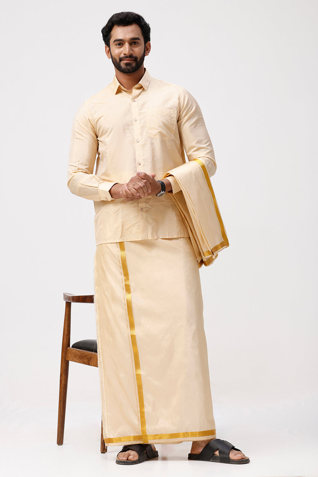 Man wearing a traditional cream outfit with gold accents on a white background