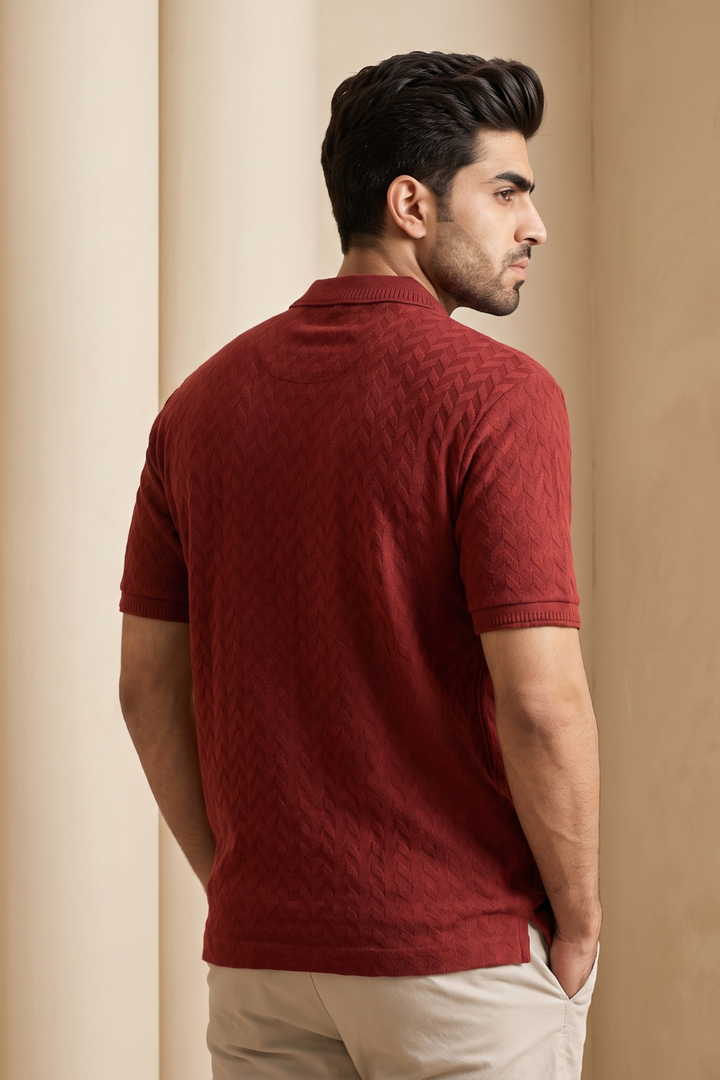 A man wearing a textured, short-sleeve knit polo shirt in deep burgundy, shown from a three-quarters back view against a warm beige background.