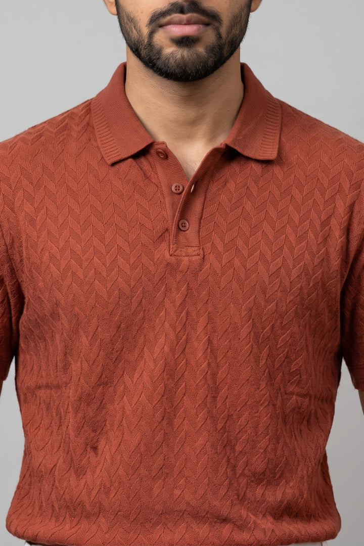 A man wearing a rust-orange textured knit polo shirt against a plain gray background.