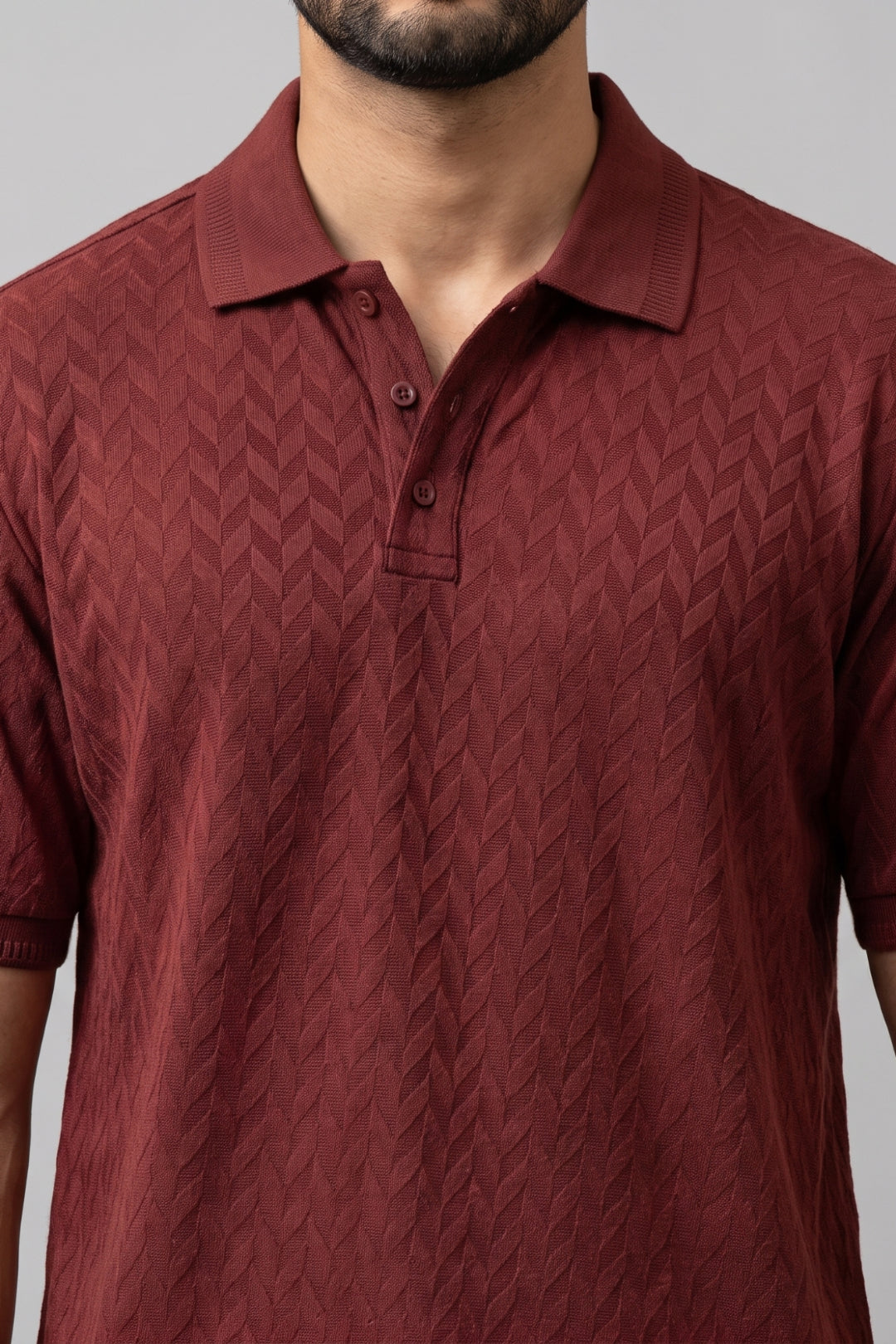 A close-up of a man wearing a short-sleeve polo shirt in a deep maroon. The T- shirt features a textured, woven chevron pattern.