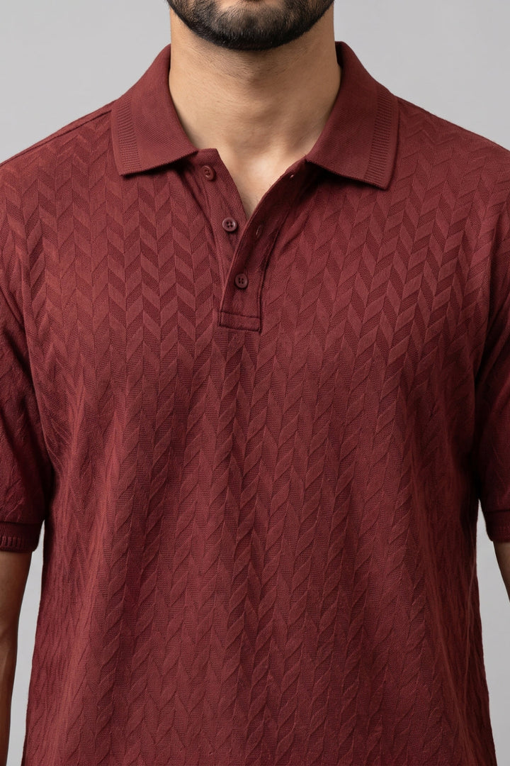 A close-up of a man wearing a short-sleeve polo shirt in a deep maroon. The T- shirt features a textured, woven chevron pattern.