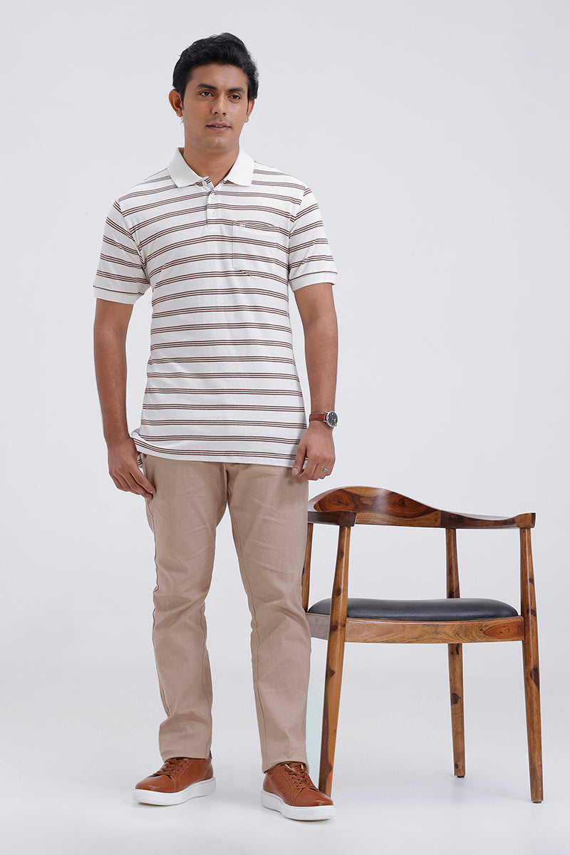 Man wearing a striped polo shirt and beige pants standing next to a wooden chair on a white background