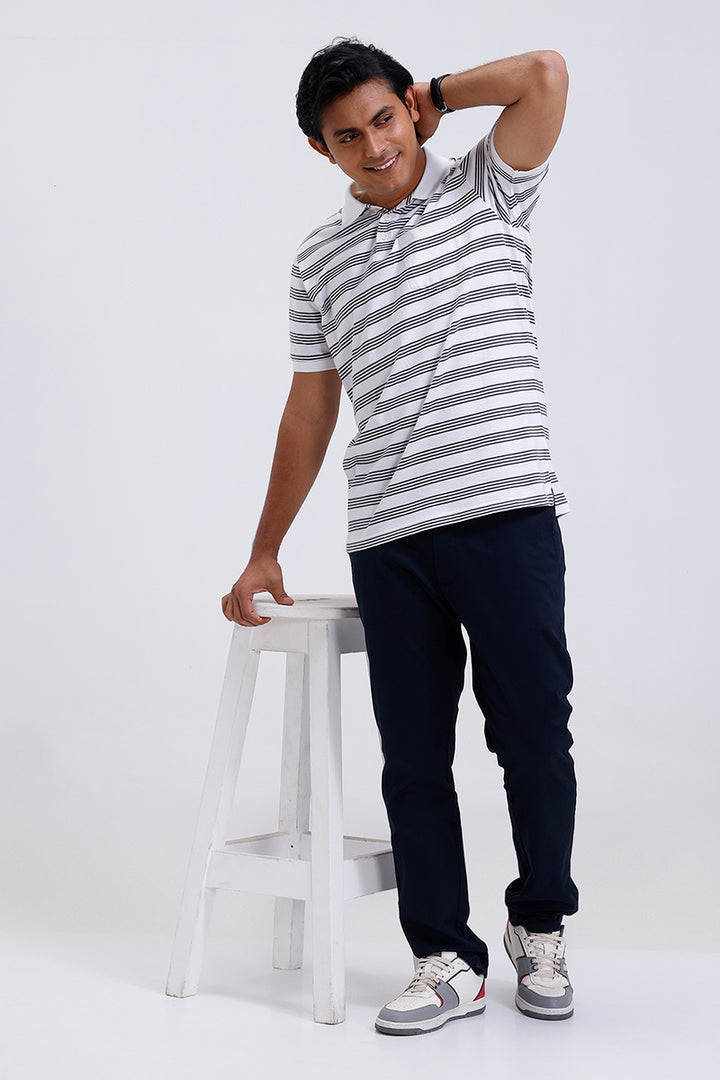 Man wearing a striped t-shirt and dark pants standing on a white stool against a white background