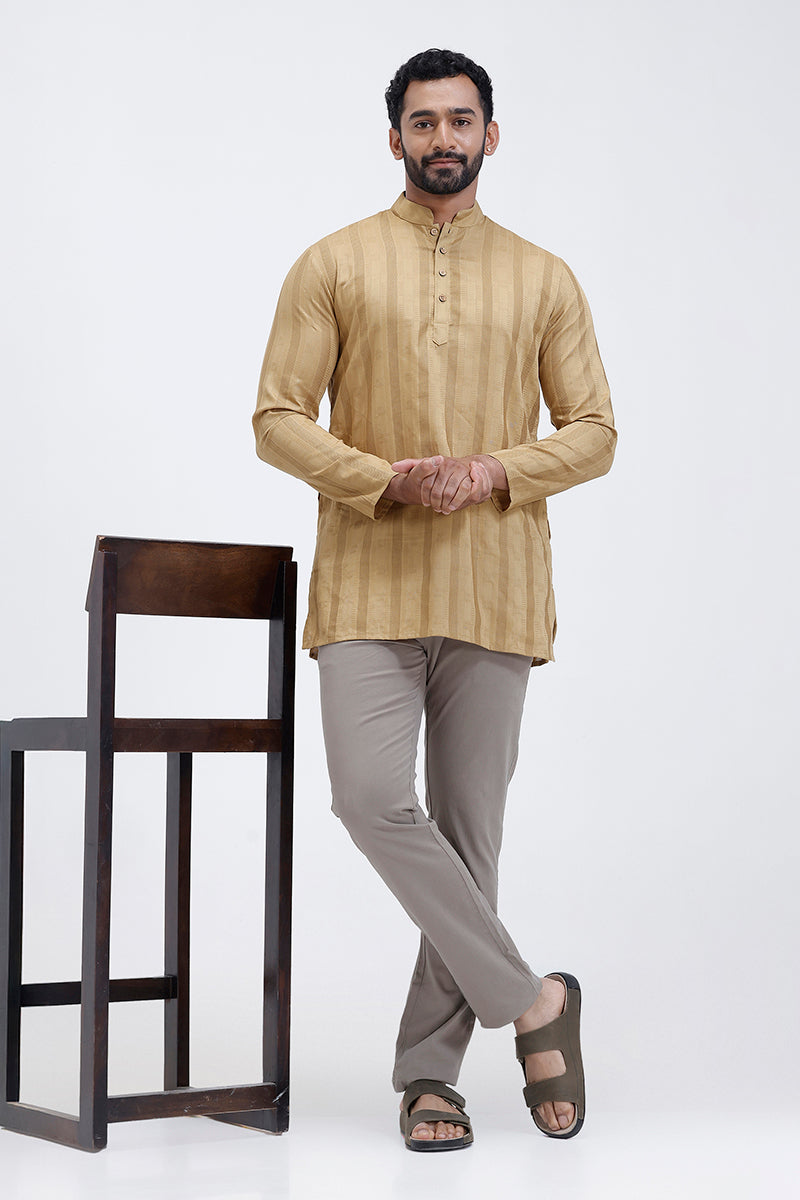 Man wearing a Mustard gold kurta with gray pants standing next to a wooden chair on a white background
