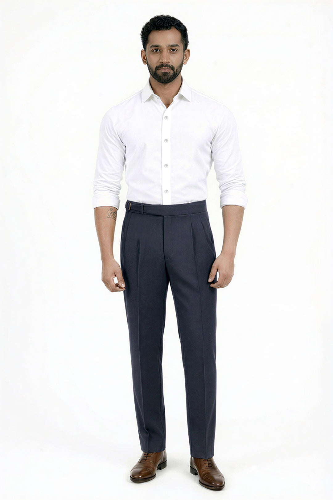 A man modeling a white long-sleeve button-down shirt and dark navy blue pleated trousers with brown leather dress shoes, standing against a plain white studio background.