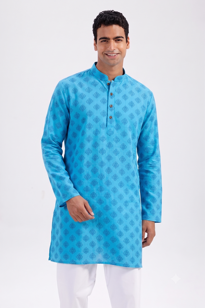 A man wearing a bright blue long-sleeve kurta with a subtle geometric pattern and white trousers, standing against a plain white studio background.