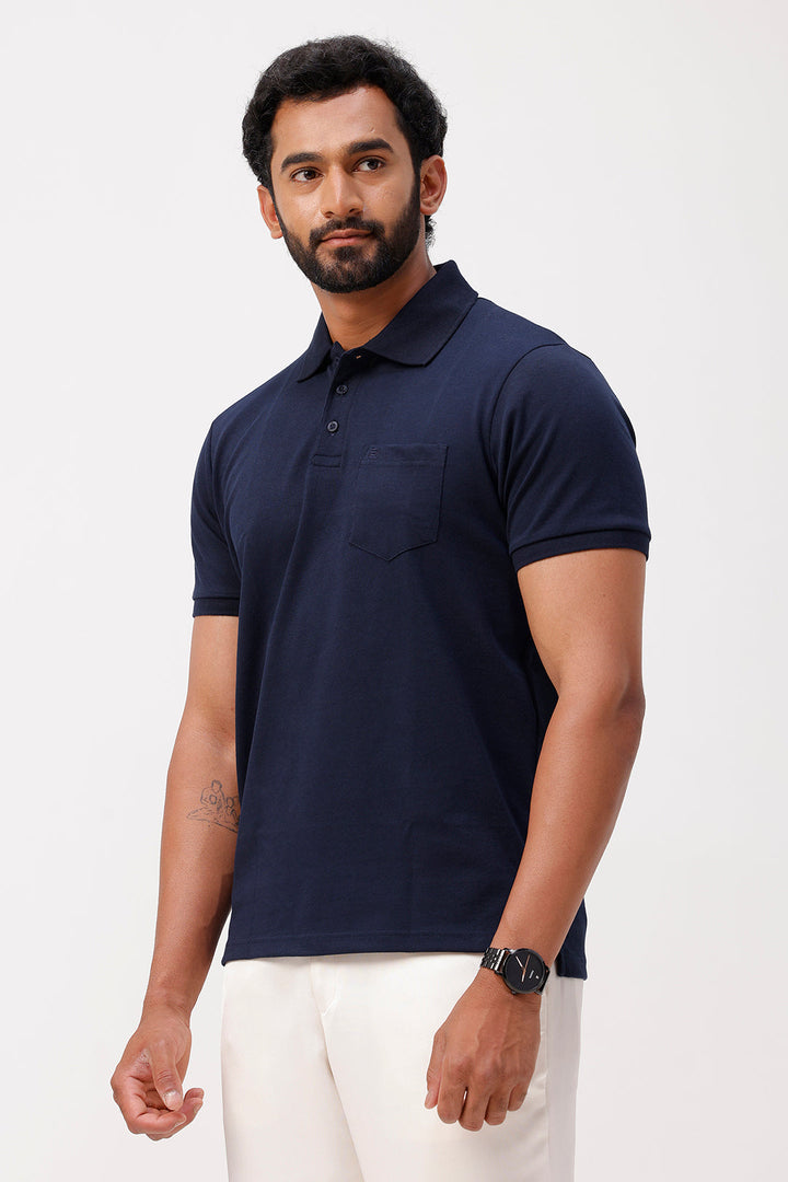 Man wearing a navy blue polo shirt and white pants on a light gray background