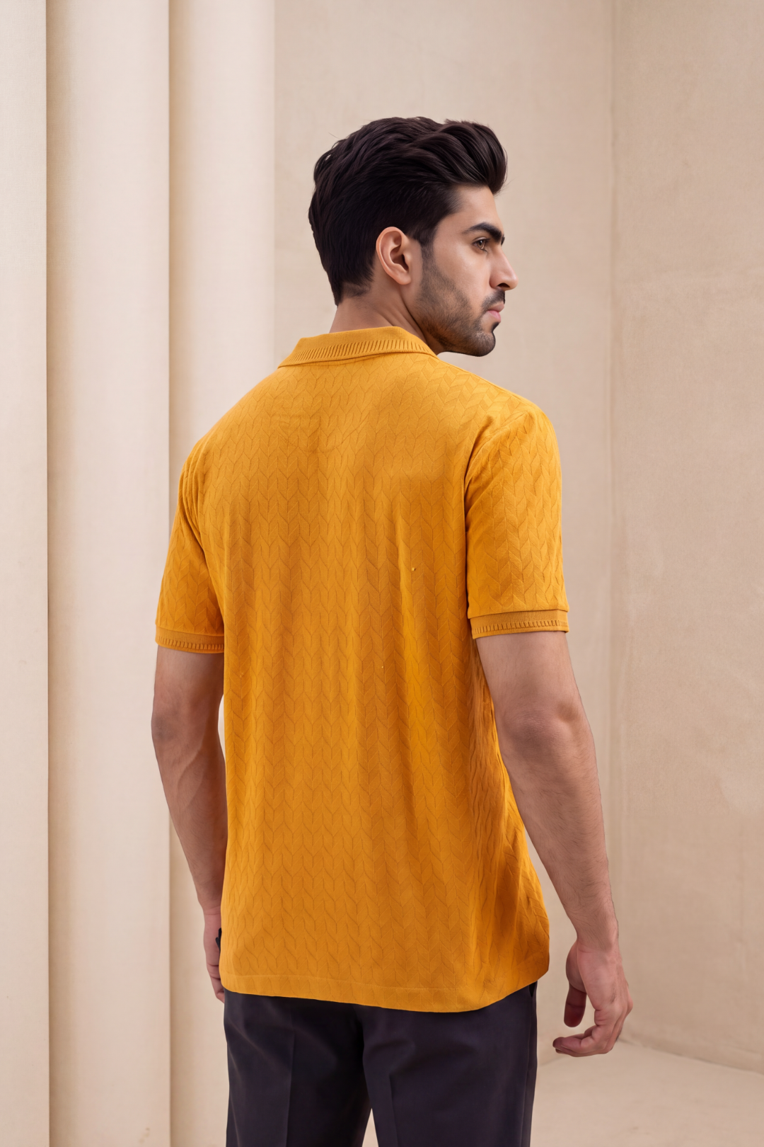 A man wearing a textured mustard yellow short-sleeve polo shirt, shown from the back and side profile against a neutral beige background.