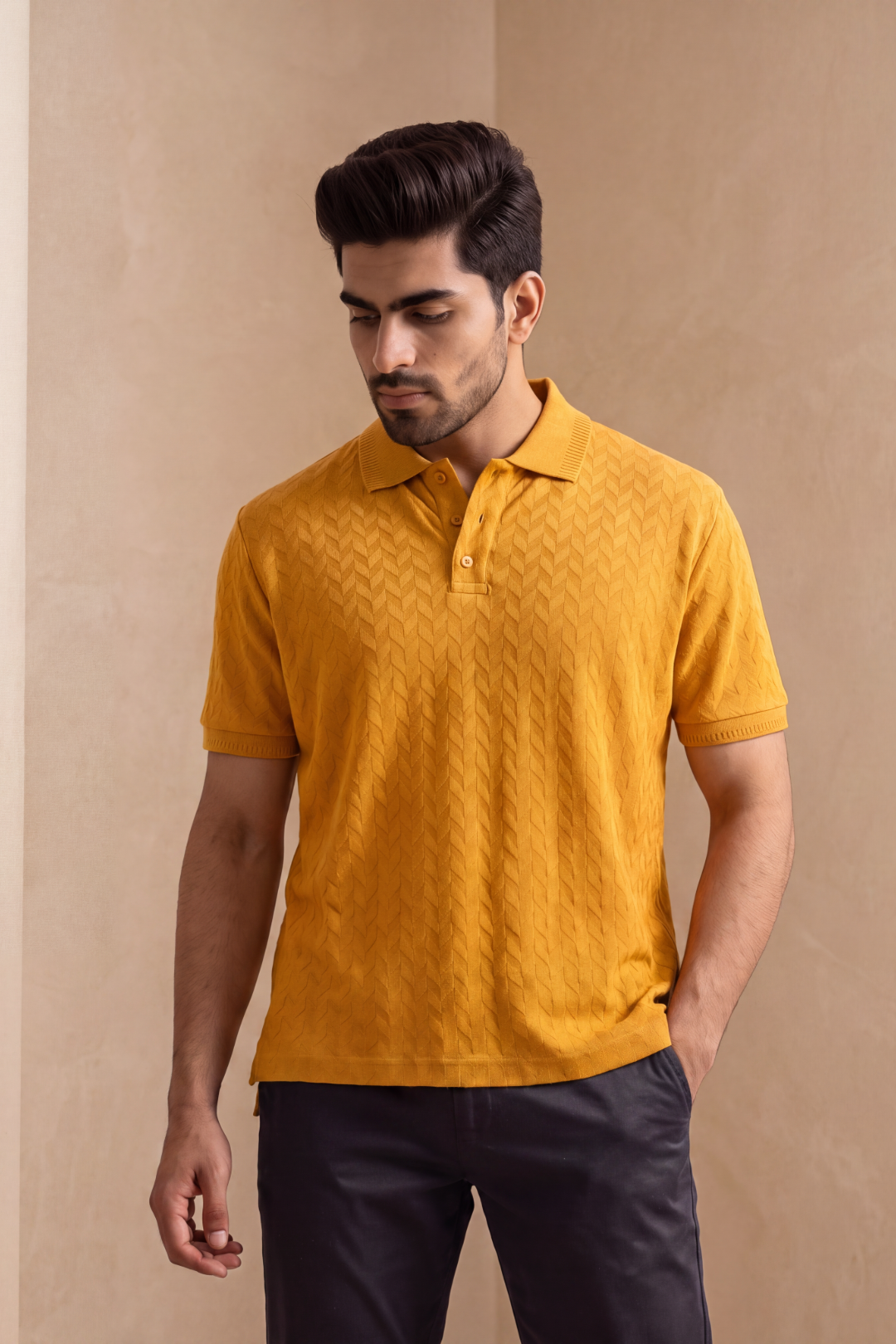 A man wearing a textured mustard yellow short-sleeve polo shirt with dark trousers, standing against a warm beige background.